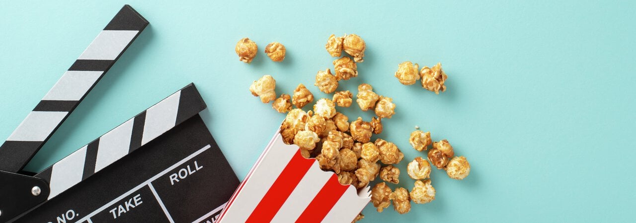 Turkis bakgrunn, i forgrunnen ser man en filmklipper og en stripede popcornkopp som det ramler popcorn ut av