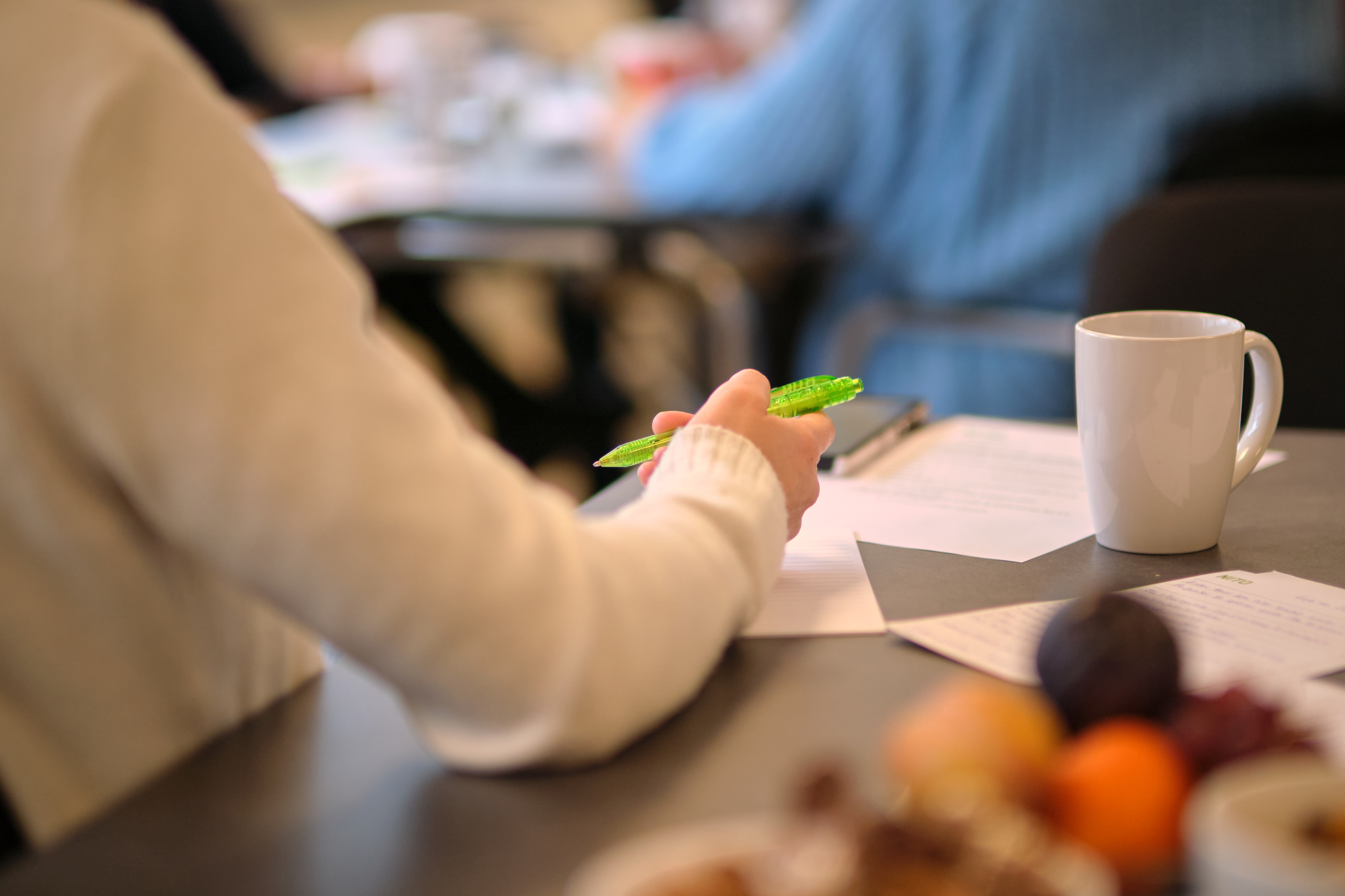 Dame som hviler hånden på et konferansebord med en penn i hånden. 