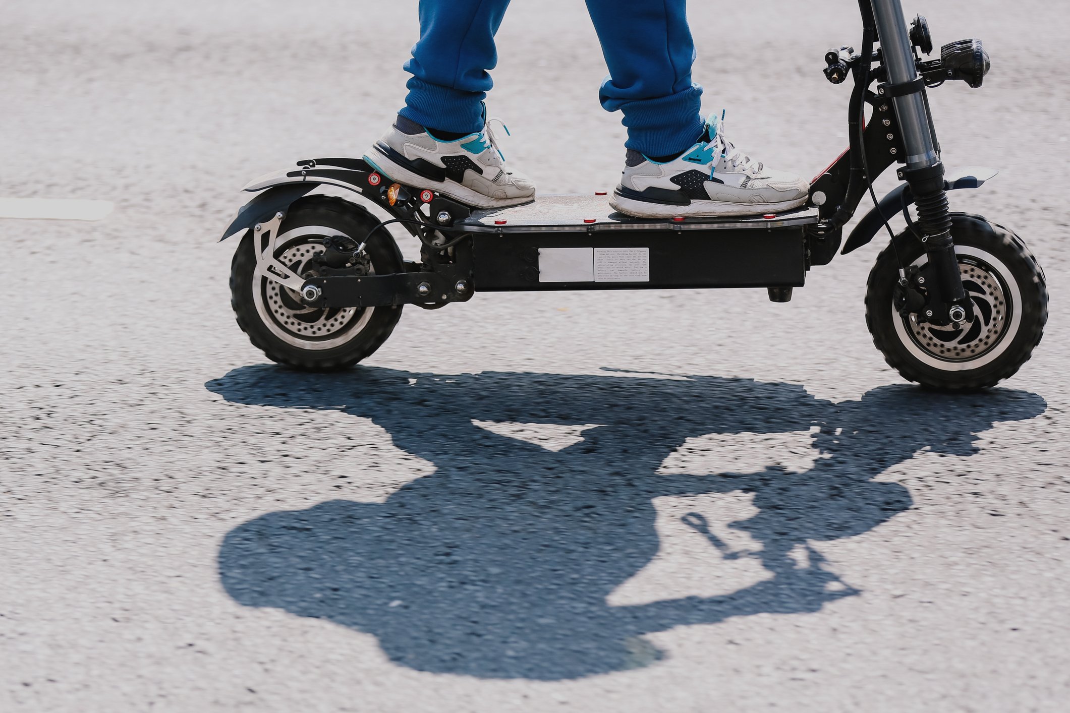 A person stands on an electric scooter on asphalt.