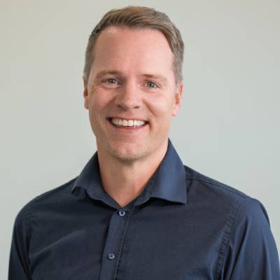 Mann i mørkeblå skjorte med kort, brunt hår. Bakgrunnen er lys og nøytral.