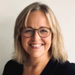 Portrett av smilende kvinne med briller og halvlangt lyst hår.