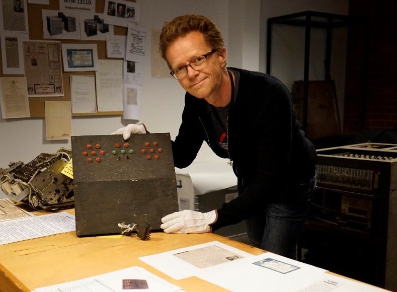 Ansatt på Teknisk museum holder opp en museumsgjenstand - Hofgaardmaskinen