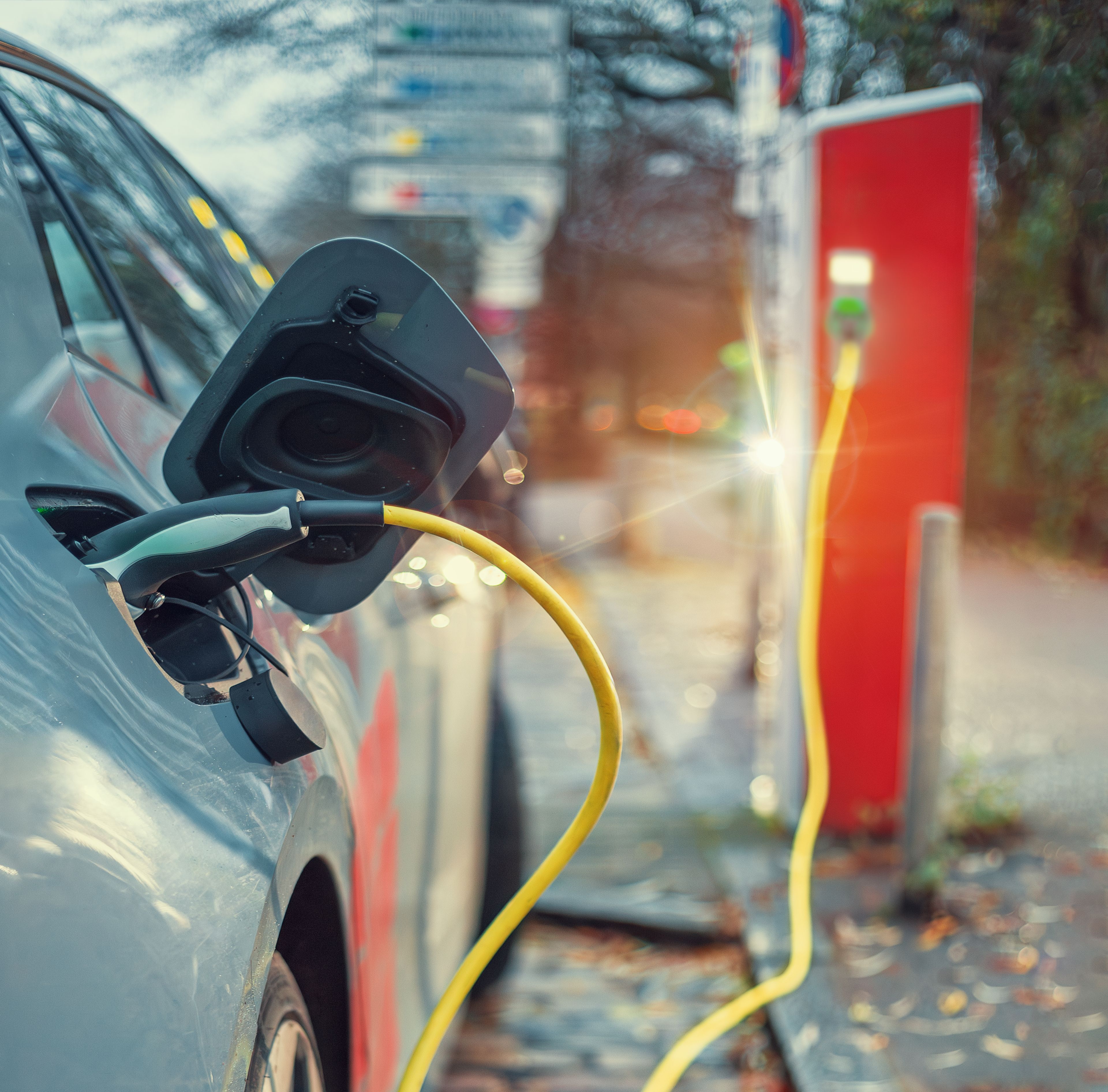 electric car that is plugged into a charging cable, with the charging tower behind the car