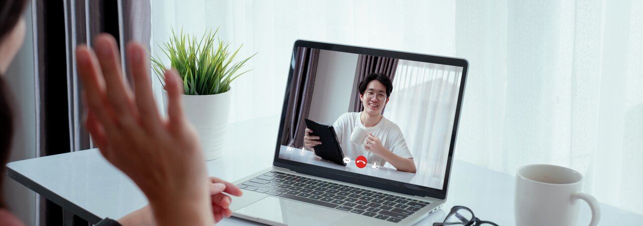 En hånd som hilser til en person på skjermen foran seg 