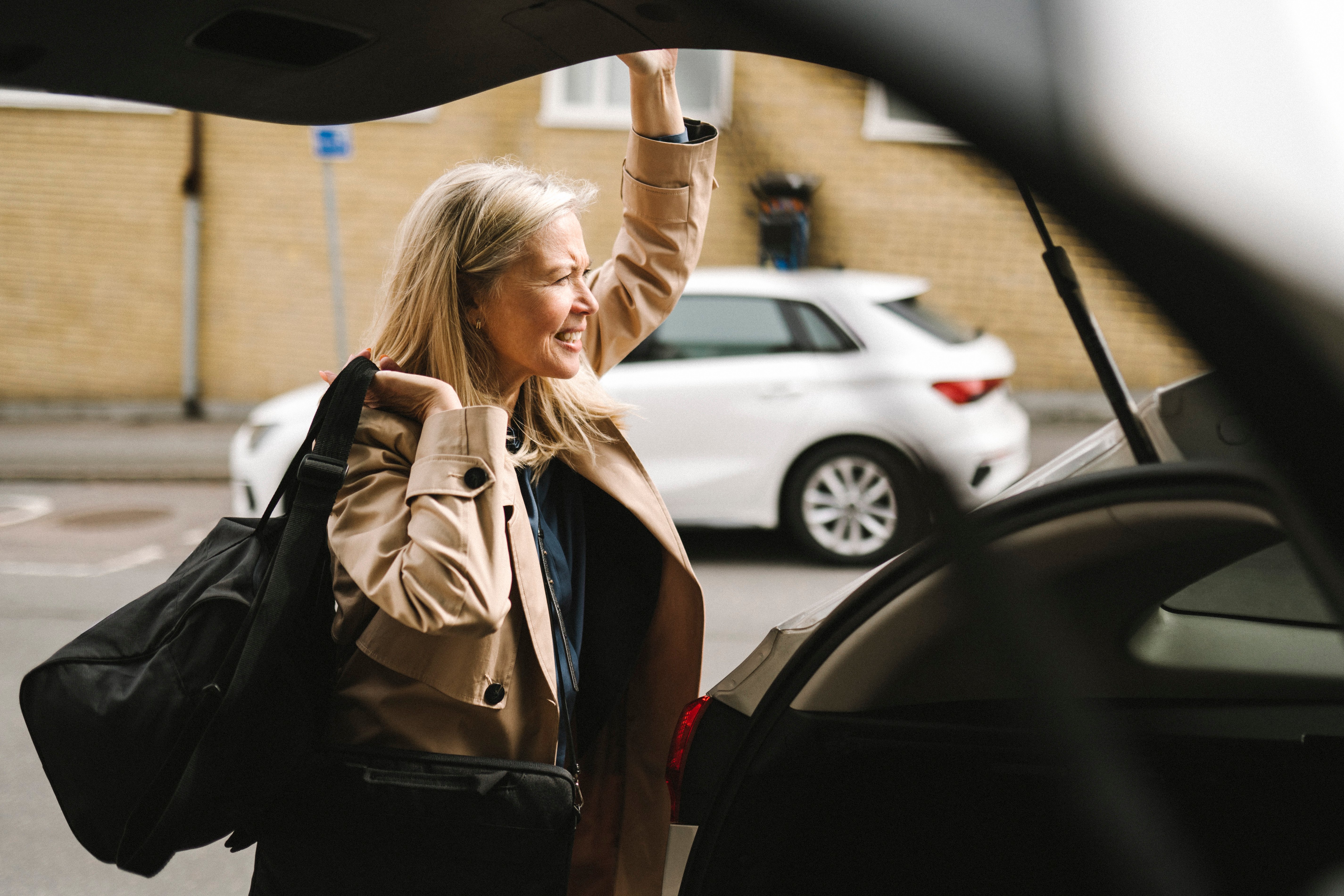 Woman with bag over her shoulder closes the trunk of the car on the way to a business trip. Photo: GettyImages