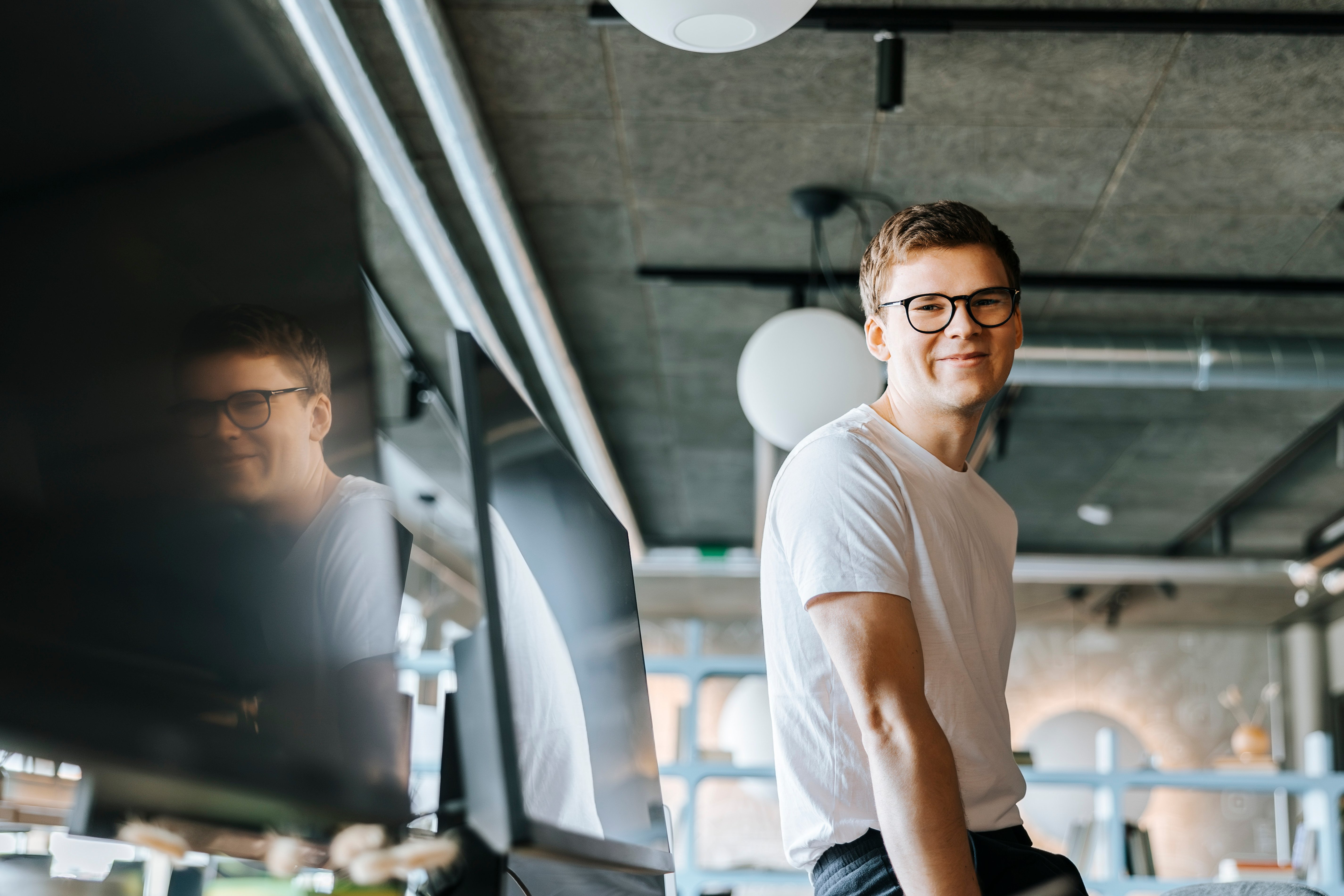 A young male engineer smiles confidently at the camera in a modern office environment.