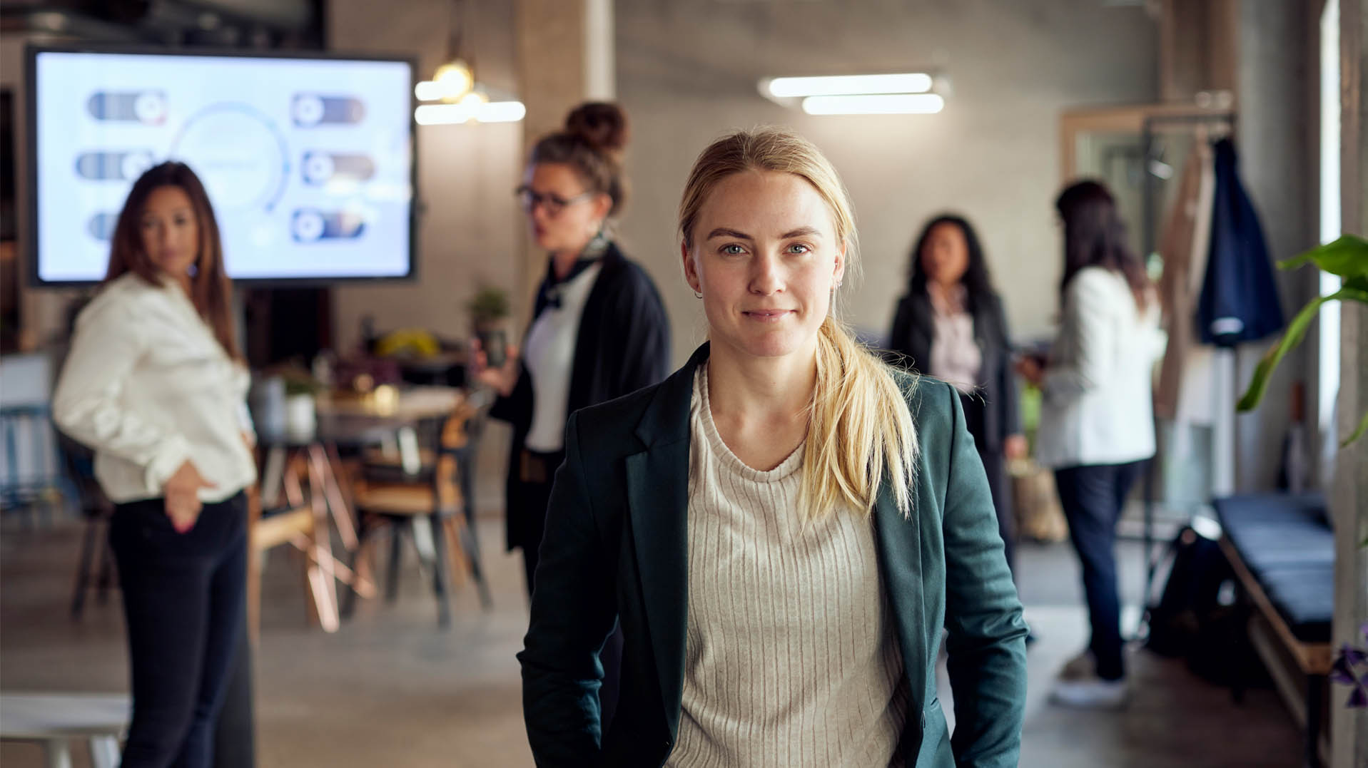 En gruppe kvinner i et moderne kontormiljø, en kvinne i forgrunnen ser selvsikkert mot kamera.