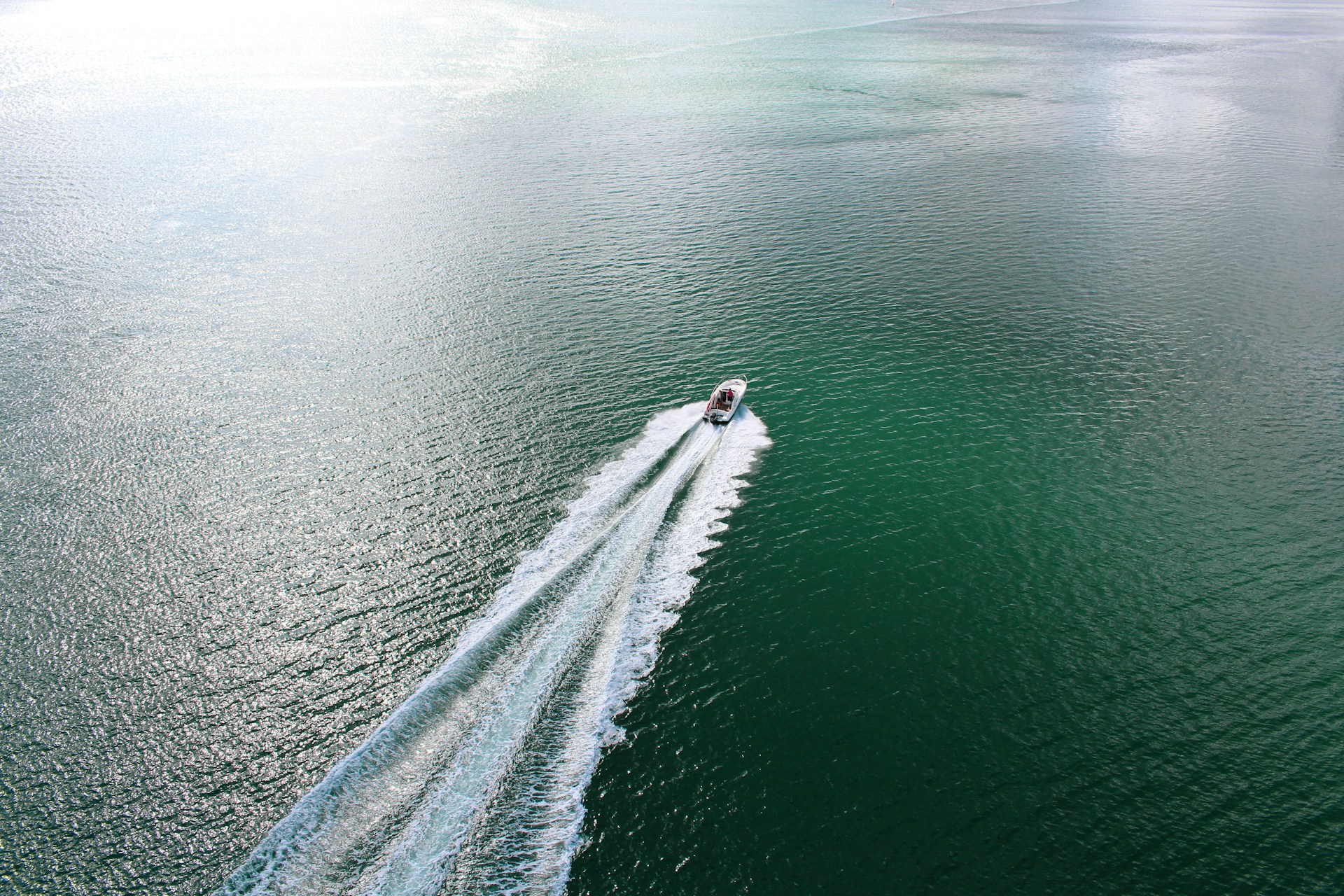 A small motorboat cuts through the water, leaving behind a white wake under the open sky.