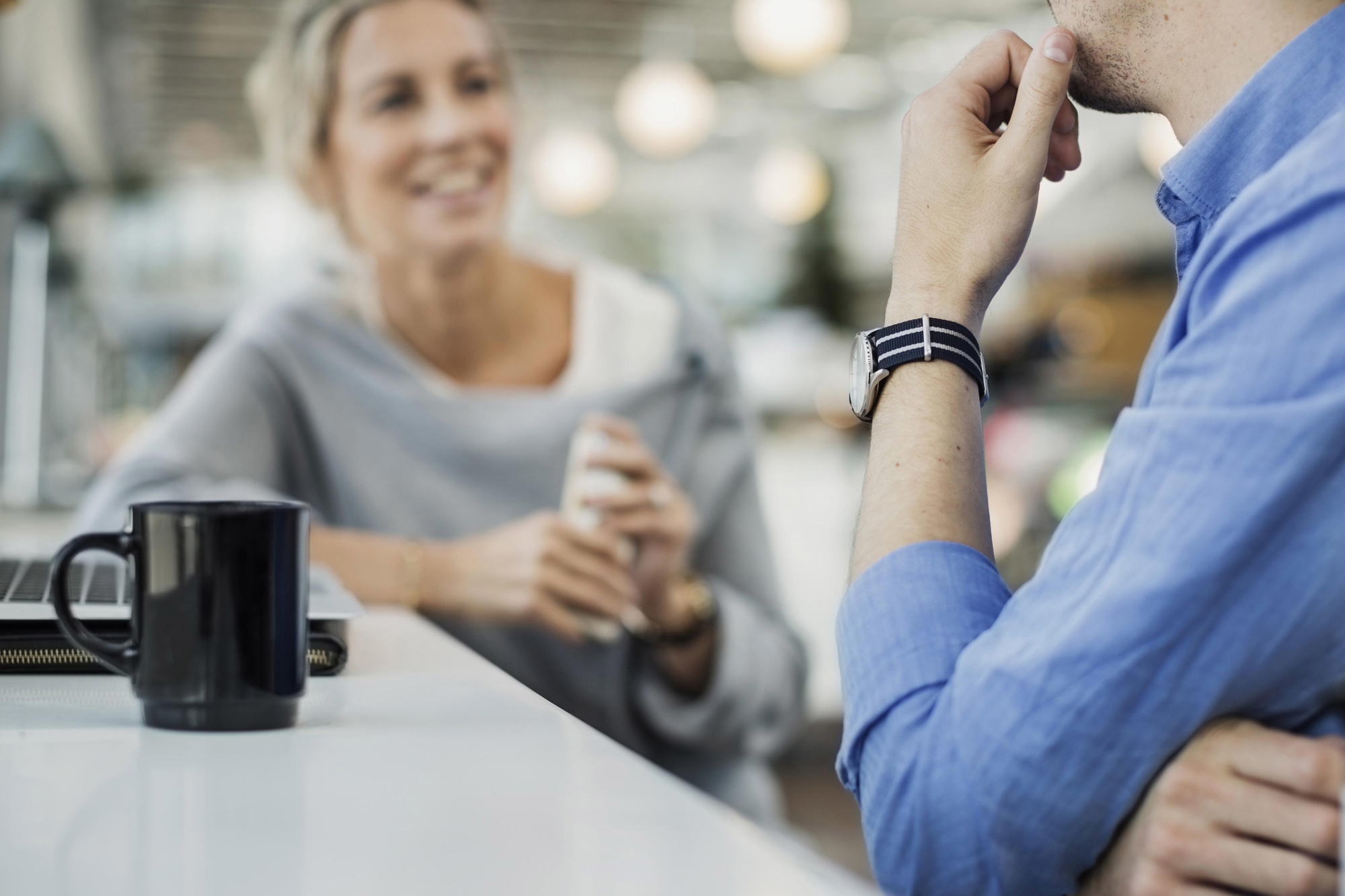 To kolleger i samtale over kaffe, der den ene smiler, illustrerer en positiv lønns- eller forhandlingssamtale.