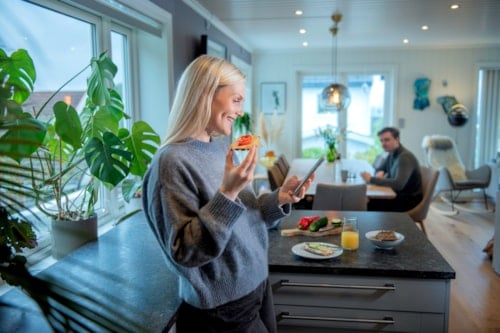 Ung dame er hjemme og ser på telefon mens hun spiser