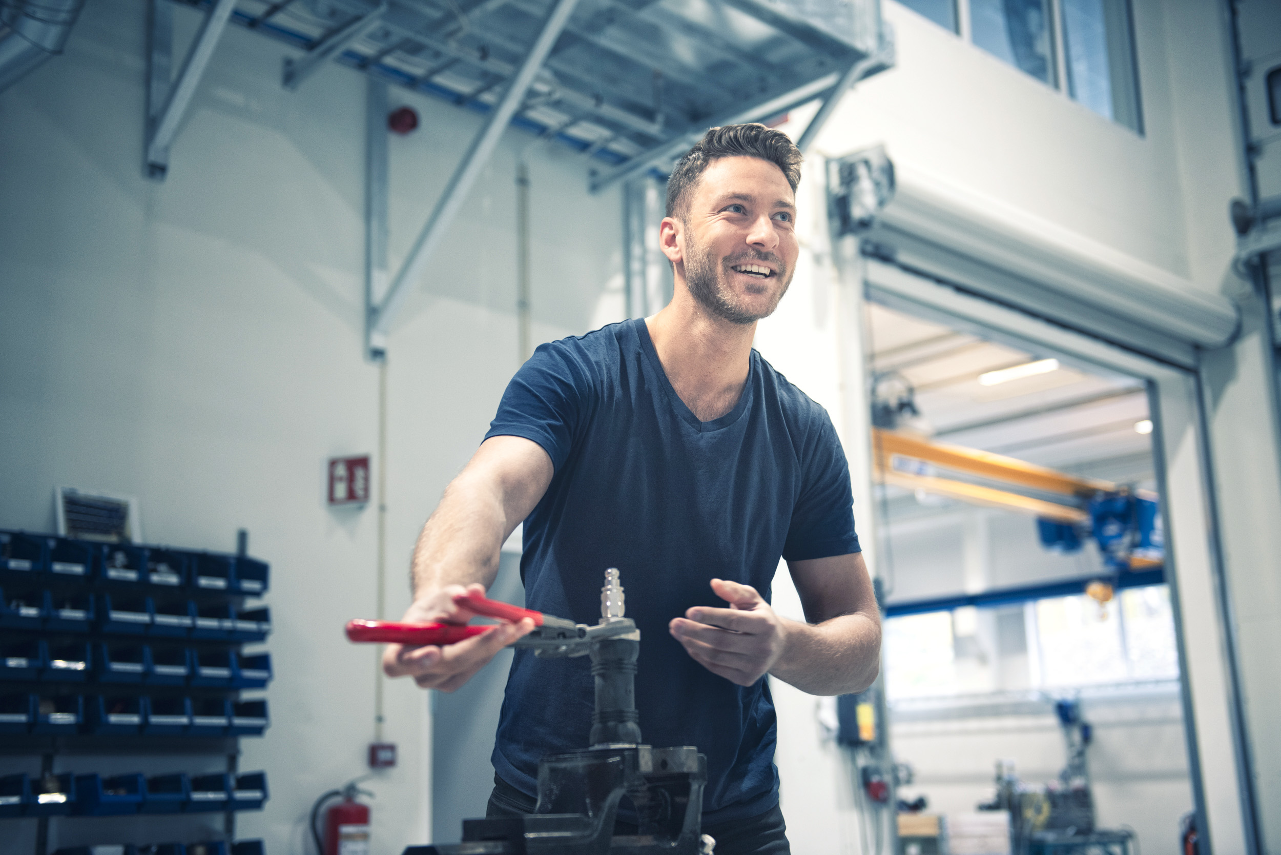 En smilende ingeniør eller tekniker i et verkstedmiljø som holder et verktøy. Illustrerer kompetanse og verdi i lønnsforhandlinger.