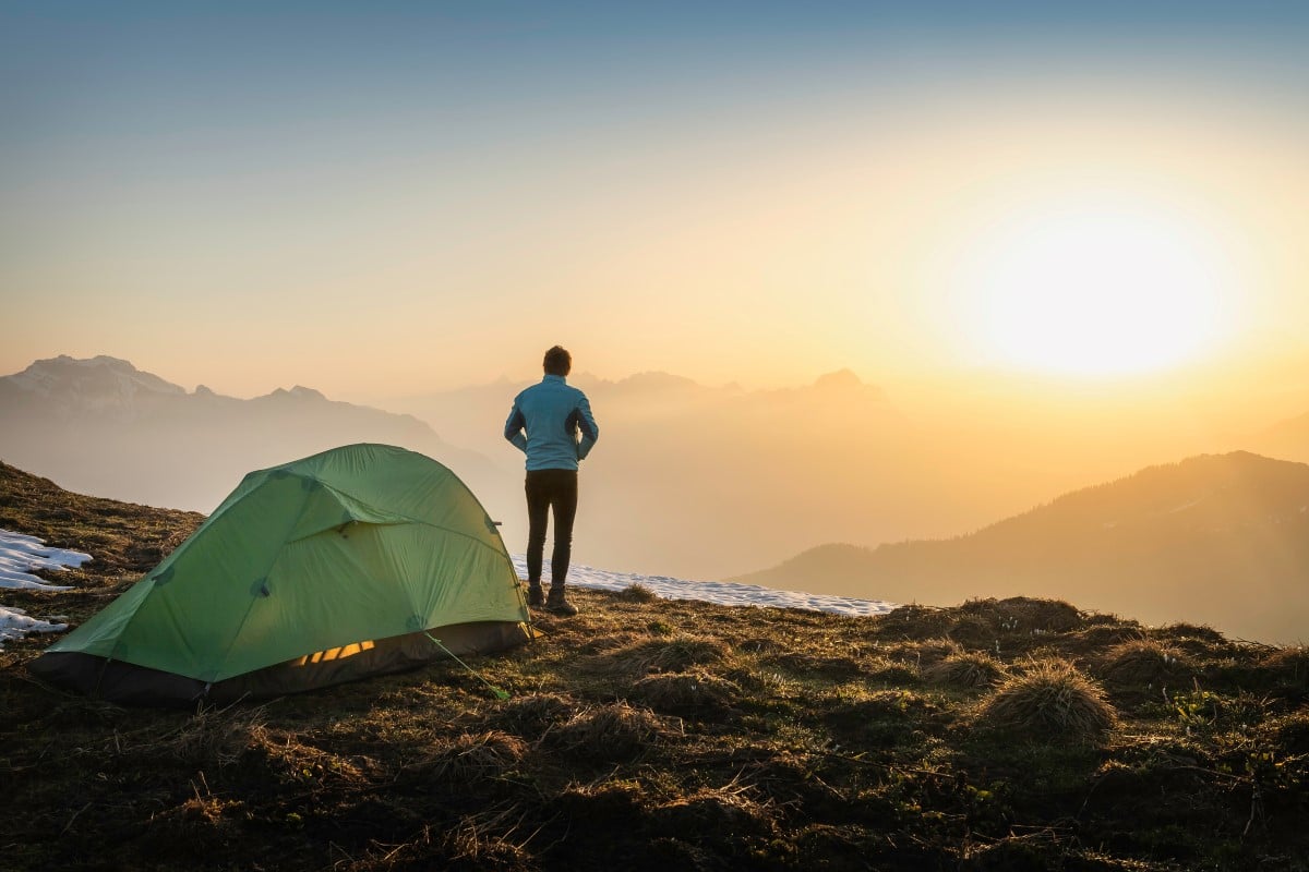 Man står ved telt og ser på solnedgangen over fjellet