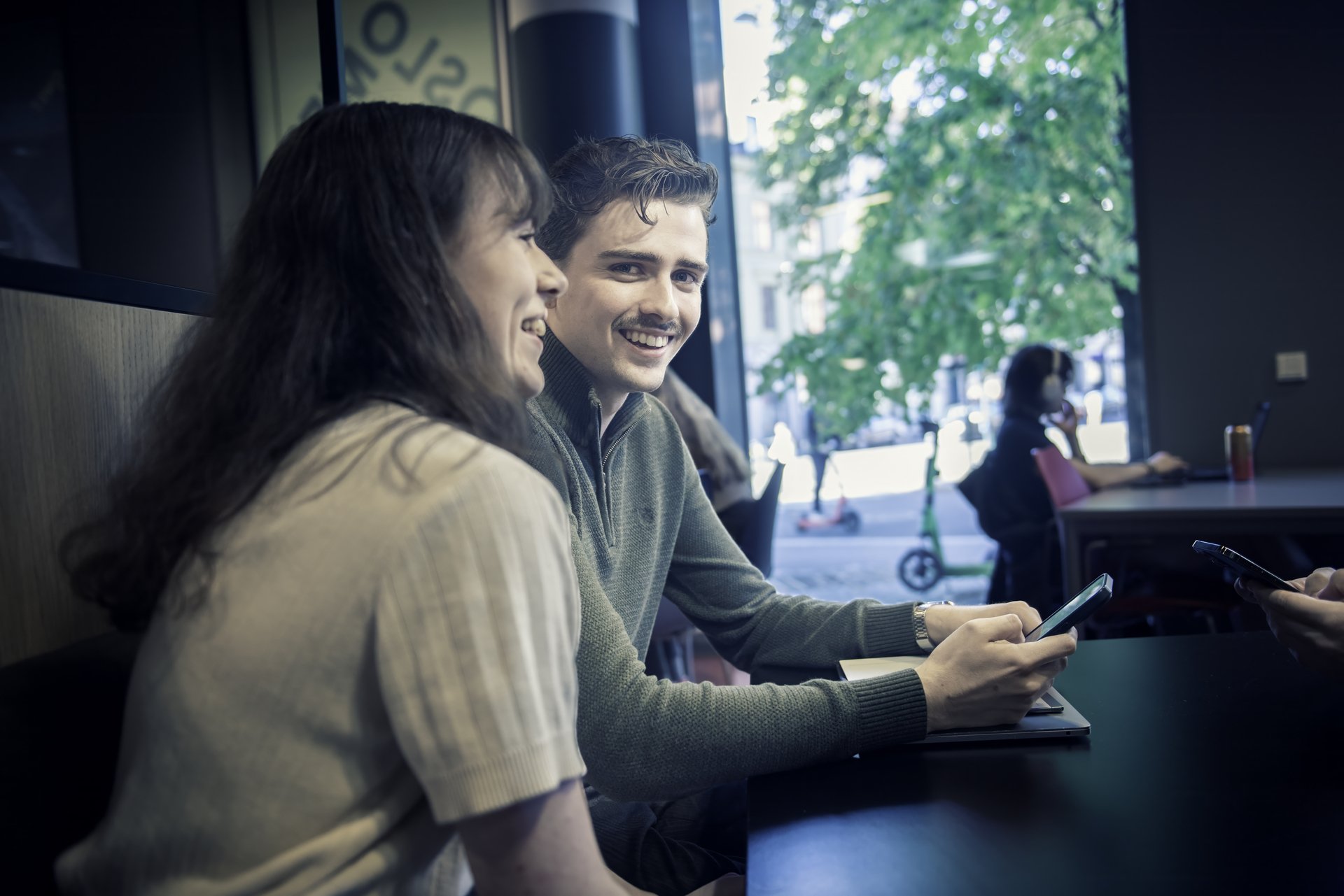 Ung mann og dame sitter ved siden av hverandre på cafe