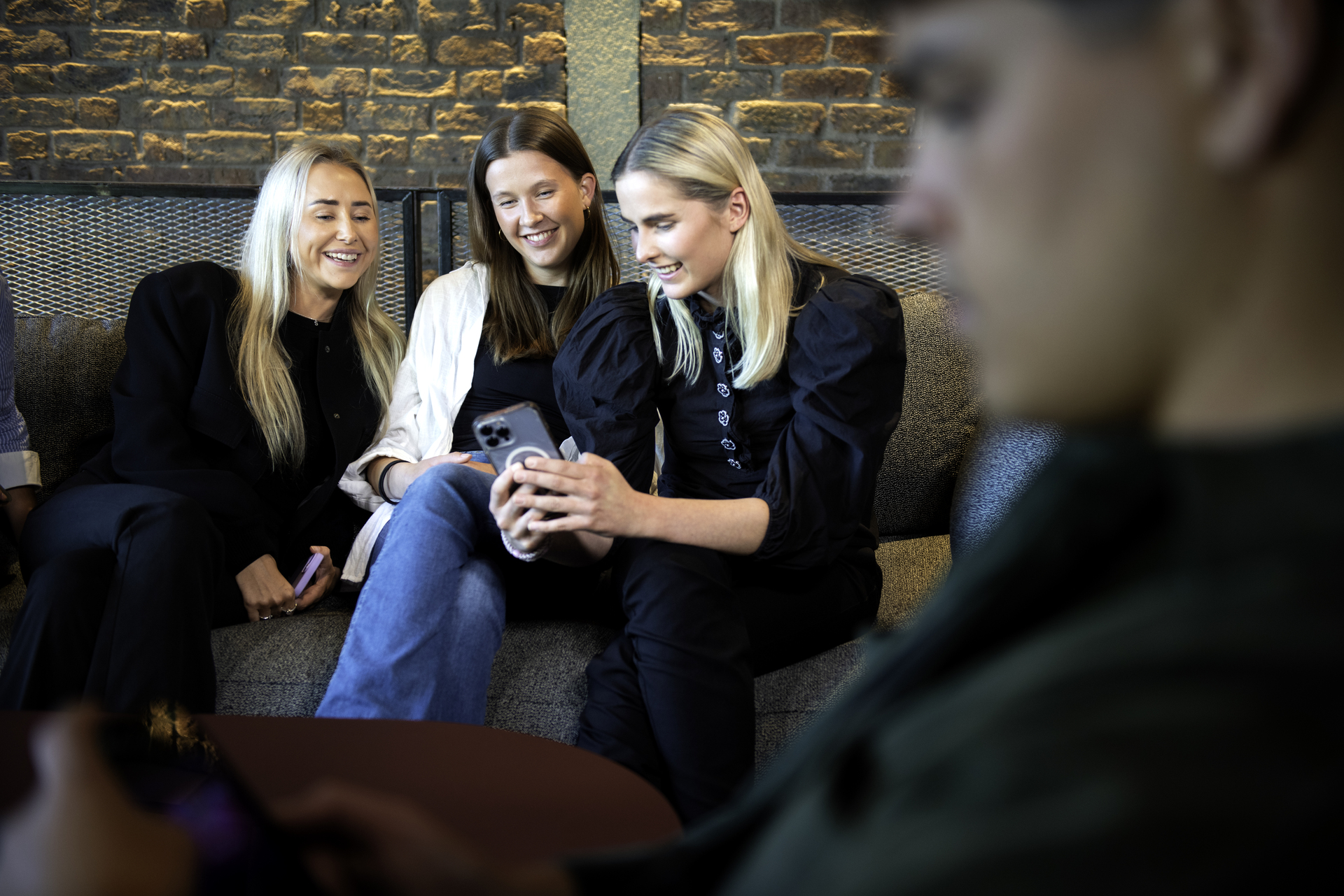 Tre unge damer sitter på en sofa og ser på en telefon