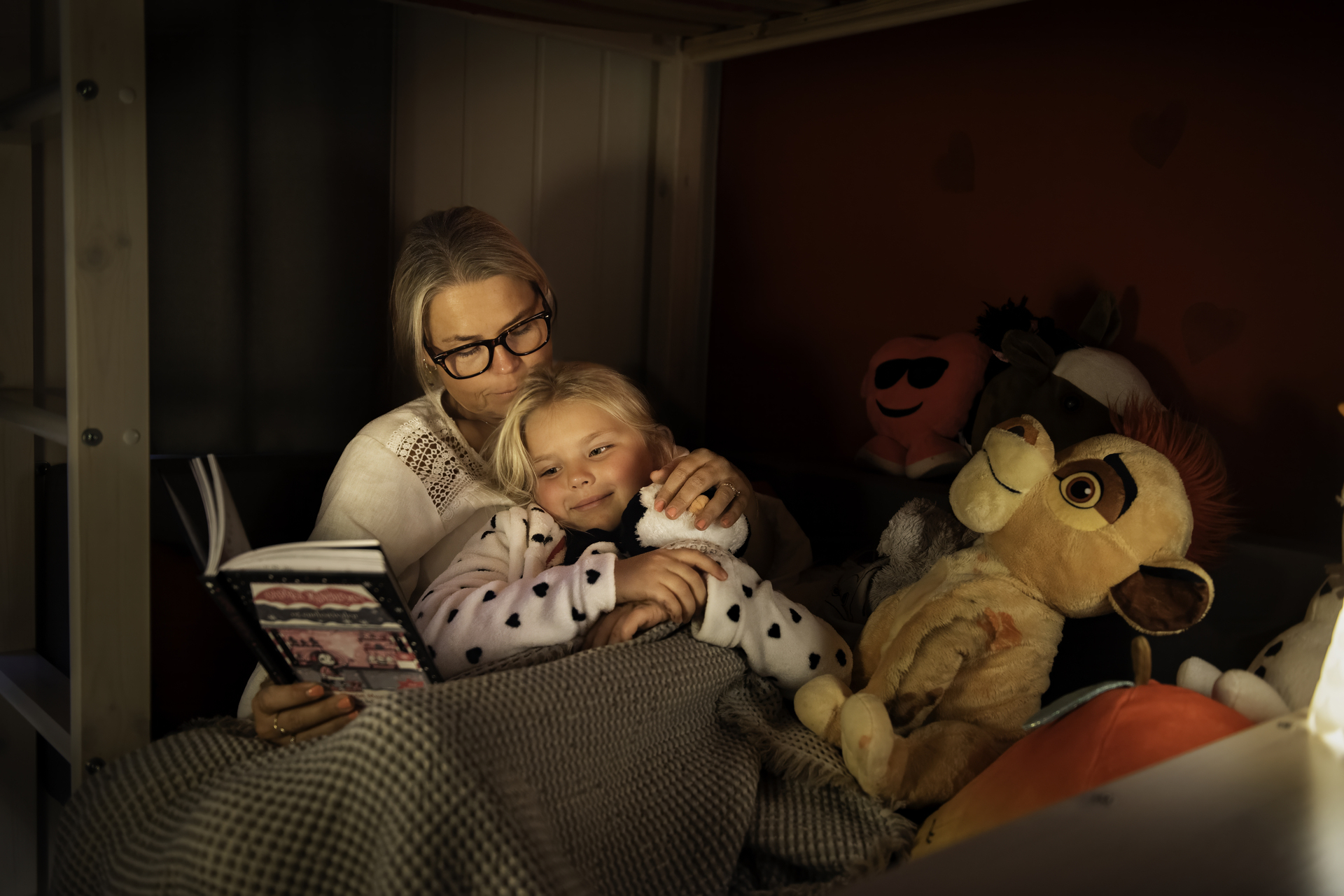 Mor og ung datter sitter i senga og leser bok