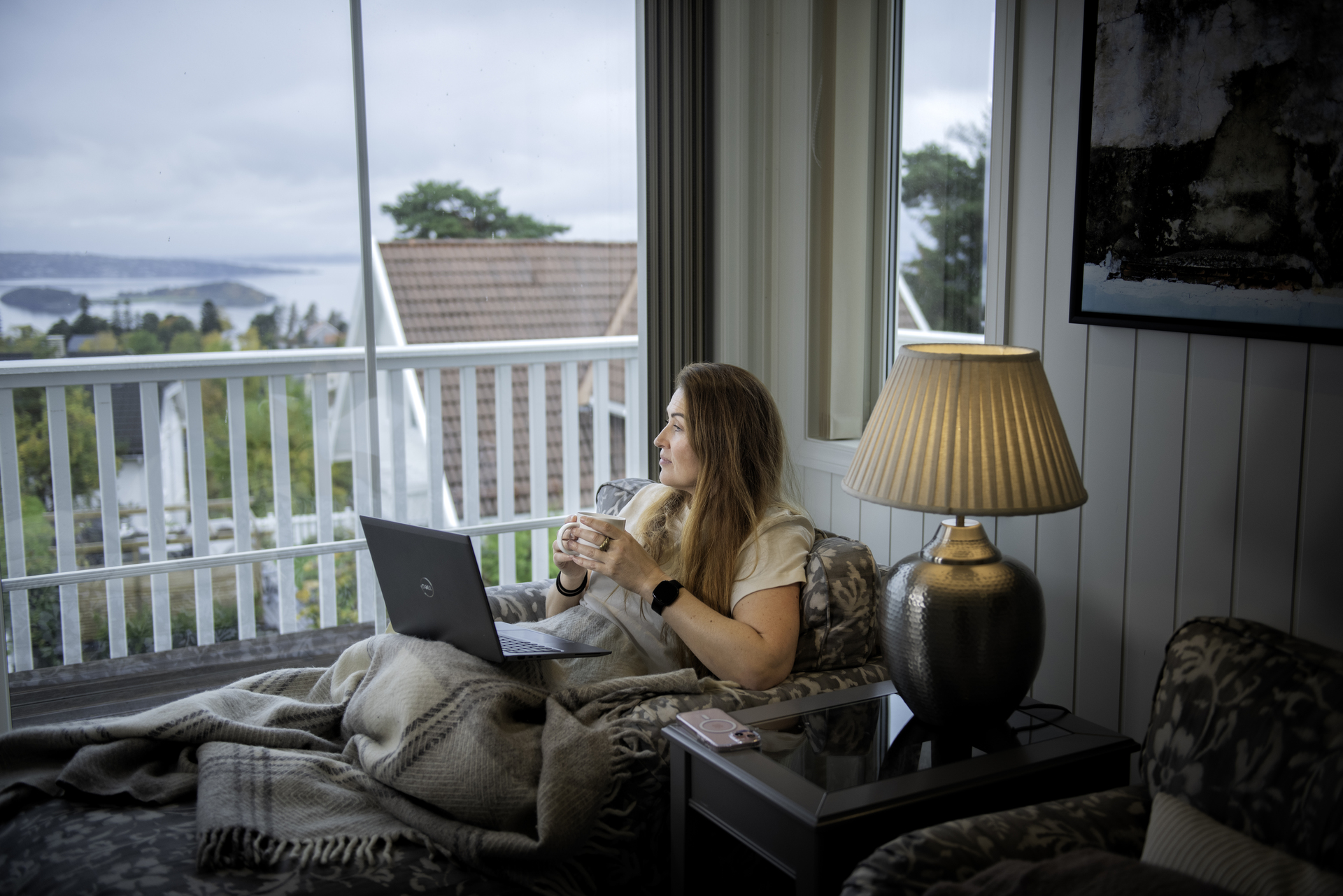 Dame sitter i sofaen og ser ut av vinduet med PC på fanget